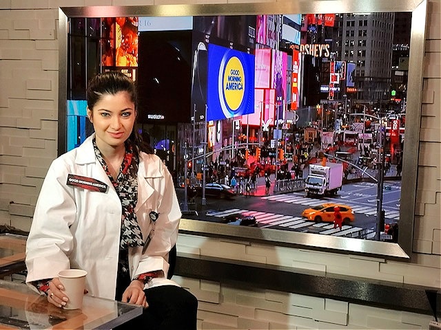 Dr. Safai in lab coat sitting backstage at GMA by window overlooking Times Square